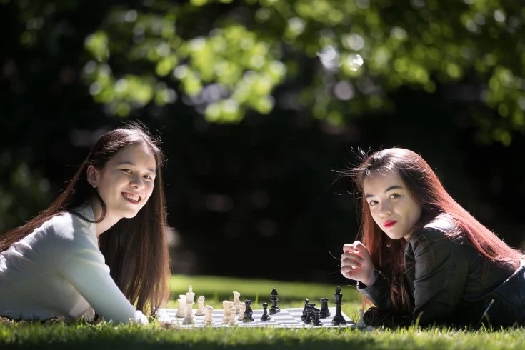 Jody Middleton and another player lying on the grass in a park, smiling on either side of a chessboard